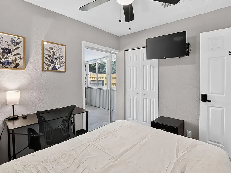 Furnished bedroom with work desk, wall-mounted TV, closet storage, and sliding-door access to a screened porch.