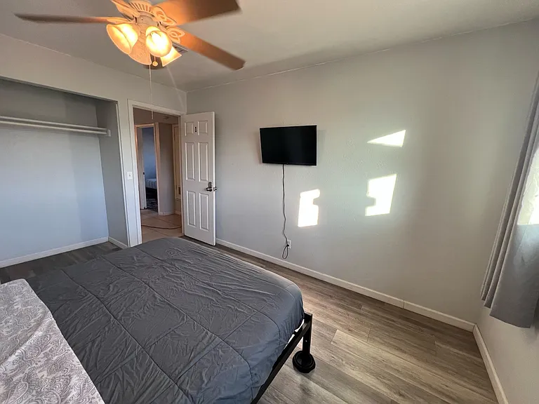 Bedroom with wood-look flooring, a ceiling fan, wall-mounted TV, and an open closet for easy storage access.