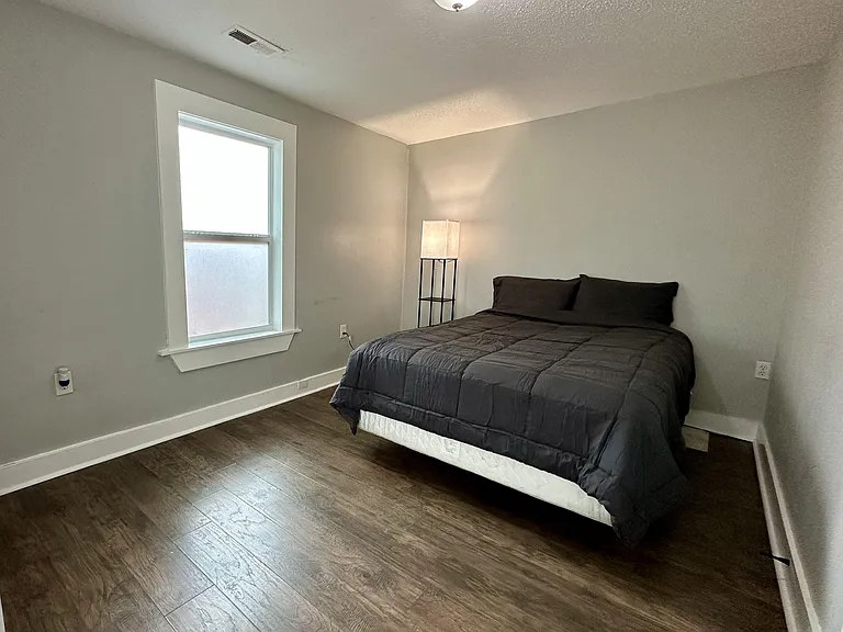 Private bedroom with wood-look flooring, a large window for natural light, and ample space for a full-size bed.