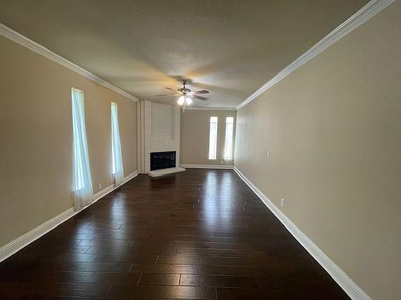 Unfurnished living room with dark wood finished floors, baseboards, crown molding, and ceiling fan