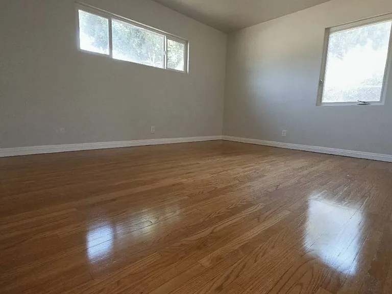 Generously sized room with refinished hardwood floors and windows on two sides.