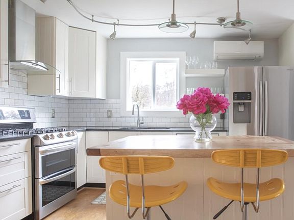Bright kitchen with white cabinets, granite countertops and stainless steel appliances. Wood topped island with seating for two.