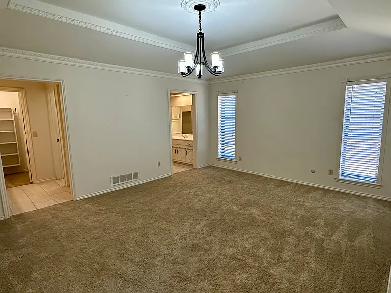 Primary bedroom with ornamental molding, an inviting chandelier with a raised ceiling, and carpet flooring