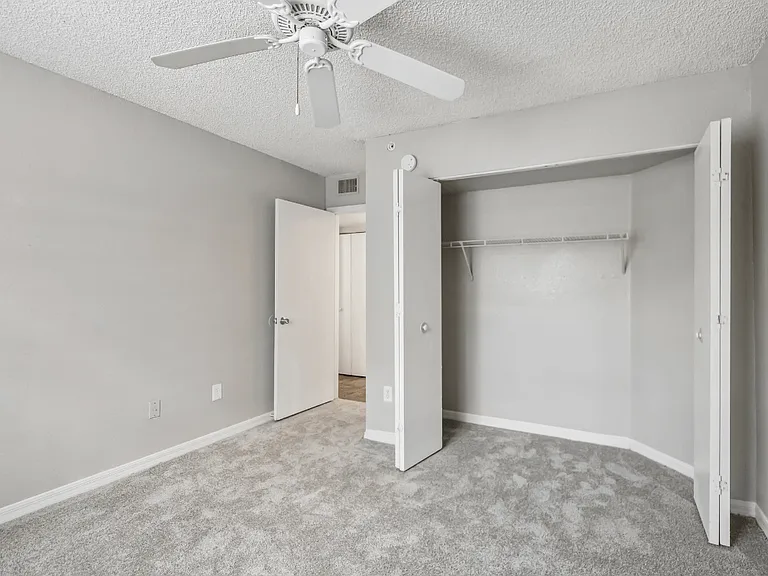 Carpeted bedroom with large closet, ceiling fan, and neutral finishes in a 3-bedroom, 2-bath apartment at Gregory Cove in Jacksonville, FL.