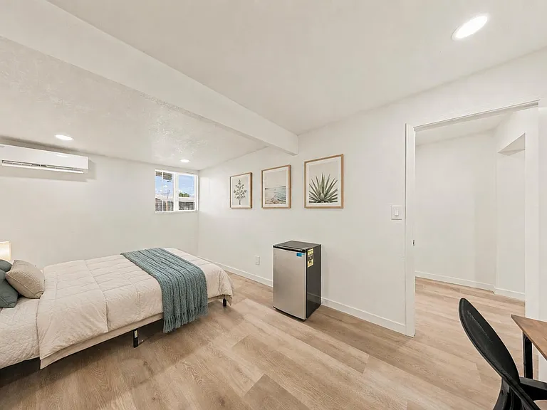 Spacious bedroom featuring wood-look floors, recessed lighting, a mini-split A/C, and a handy in-room mini fridge.