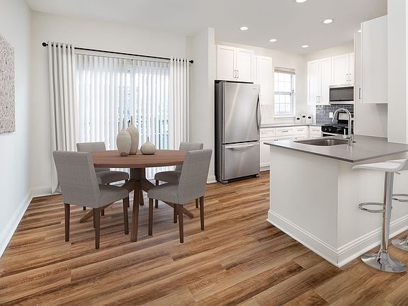 Kitchen and dining with white cabinetry, grey quartz countertops, grey tile backsplash, stainless steel appliances, and hard surface flooring