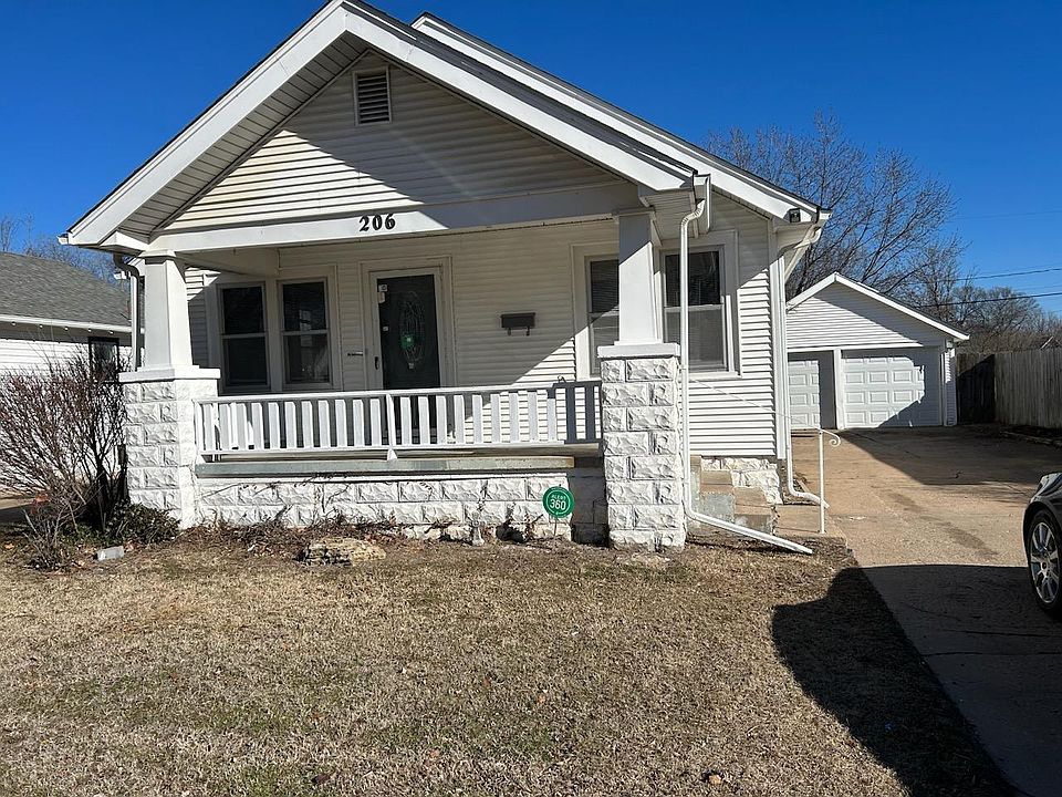 Front of house with a yard, covered patio, long driveway and 2 car garage in the back.