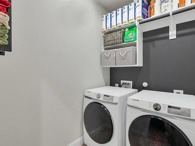 Dedicated laundry area featuring white washer and dryer units, overhead built-in shelving, and a dark accent wall