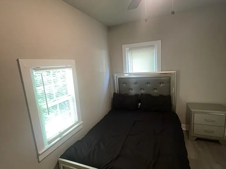 Furnished bedroom with a full bed, nightstand, and ceiling fan, plus a window with blinds for natural light.