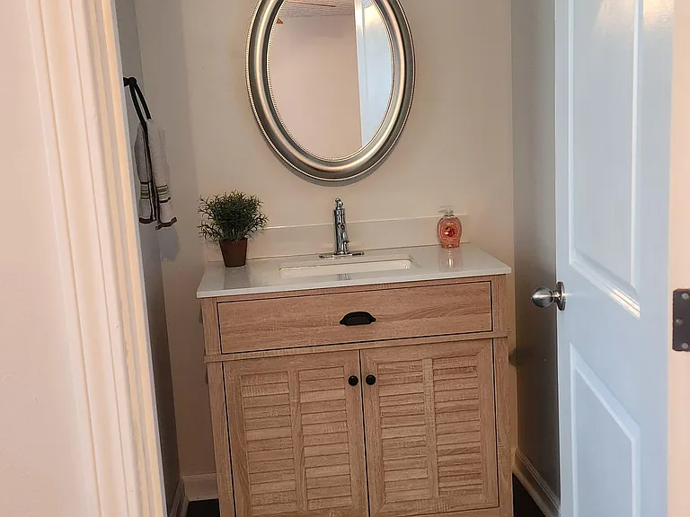 Compact bathroom vanity area with a single-sink cabinet, oval mirror, and updated overhead lighting for daily routines.