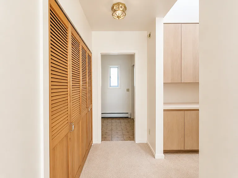 This is the view from the kitchen/entry down the hall to the bathroom ahead and storage area with cabinets and high windows to the right.