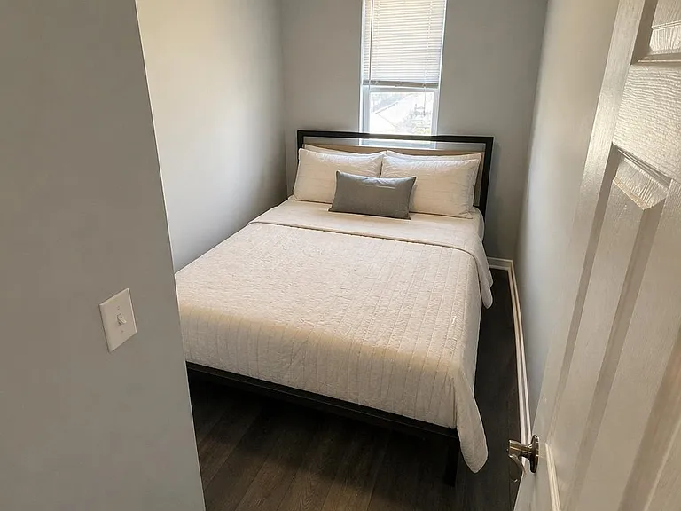 Private bedroom with a full bed, dark wood flooring, and a window with blinds for natural light and privacy.
