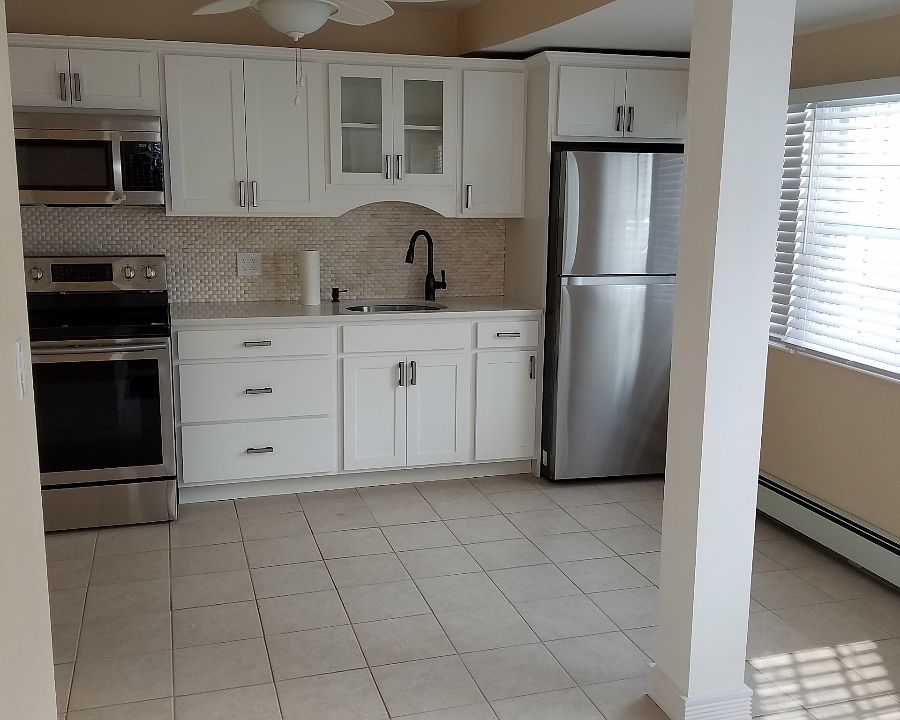 Beyond the livingroom is the kitchen, white cabinets, quartz counter tops, stainless steel appliances.