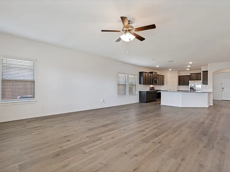 Expansive open-concept living area featuring wood-finish flooring, a ceiling fan with integrated lighting, and recessed ceiling lighting