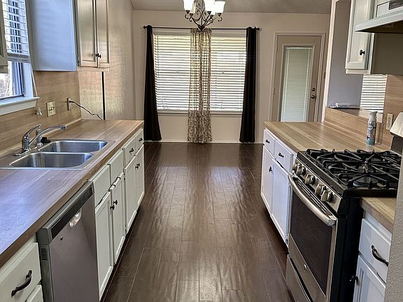 Kitchen view from garage entrance. Dining area under light fixture next to double window.