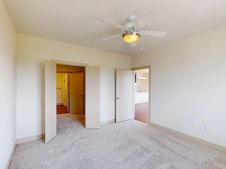 Spacious apartment bedroom with large closet, attached bathroom and plush carpet flooring.