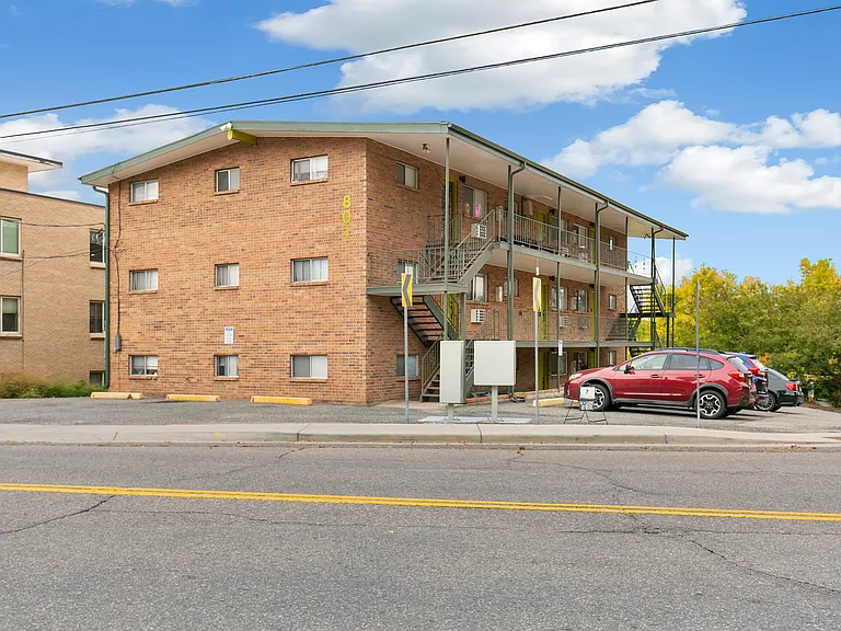 Charming three-story brick apartment building with convenient outdoor staircases and ample parking, set against a bright blue sky.