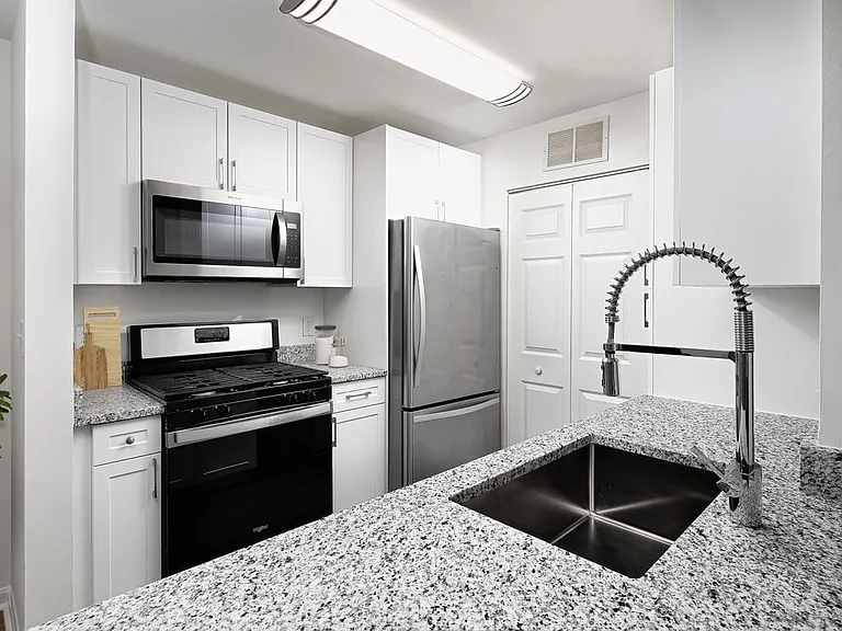 Phase I Renovated apartment kitchen with stainless steel appliances, grey speckled granite countertop, and white cabinetry