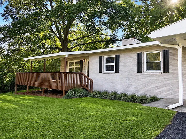 Angled view of the brick exterior, raised front deck, landscaping and covered carport.