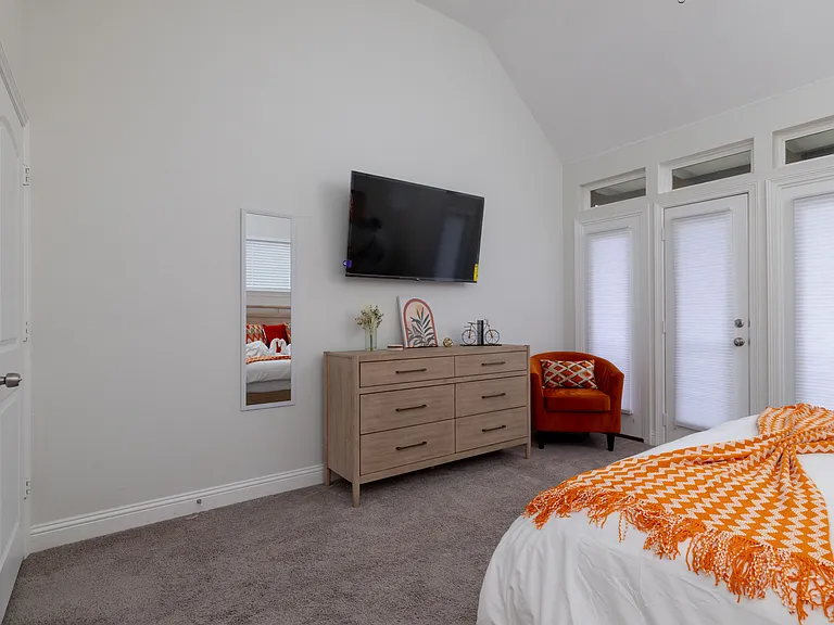 Primary bedroom features a king-size bed, corner chair, wall-mounted TV, backyard access, and an attached bathroom_your private retreat for comfort and relaxation.