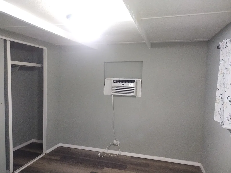 Master bedroom with AC window unit, new laminate flooring and closets, also a window to the right with new curtains