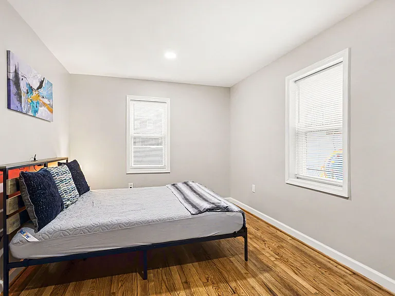Private bedroom with hardwood floors, a full-size bed setup, and two windows with blinds for natural light and privacy.