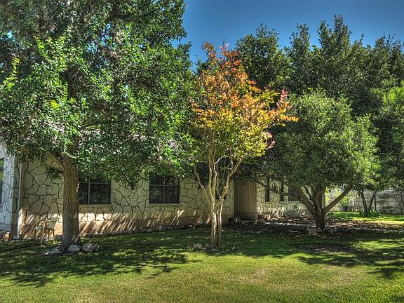 Stone veneer exterior with multiple window openings, surrounded by mature trees and a manicured lawn