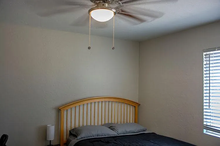 Bedroom with a bed setup, ceiling fan with light, and a window with blinds for adjustable privacy and daylight.