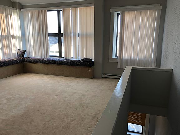 The west-facing great room, bathed in natural light features a LBFP, wall-to-wall carpeting, 15' ceiling and lovely window seats under a bank of windows