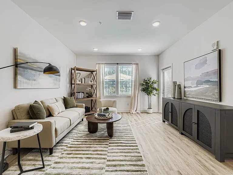 Bright and modern living room featuring a cozy beige sofa, stylish artwork, and abundant natural light from large windows.