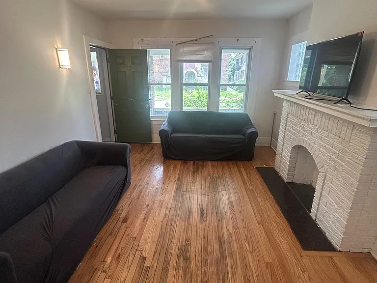Living room with hardwood floors, ample windows, and a decorative fireplace mantelideal for shared lounging and TV setup.