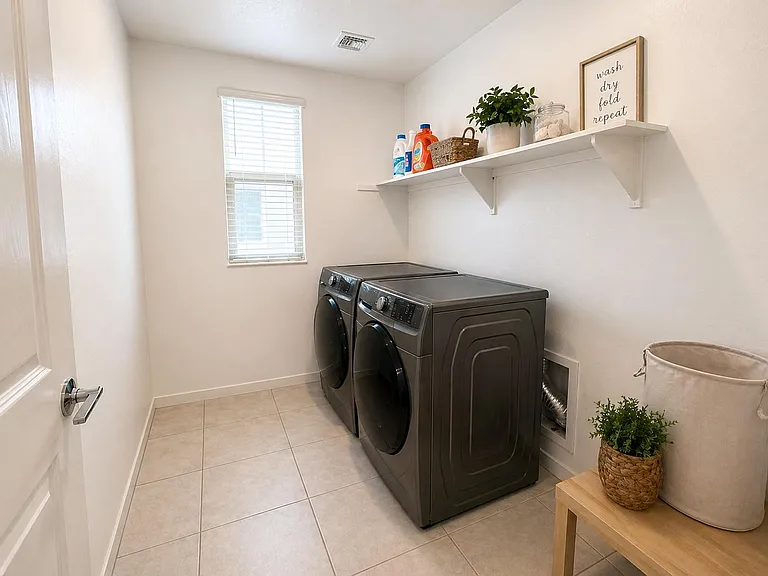 Dedicated laundry room with front-load washer and dryer, tile flooring, shelving for supplies, and a window for ventilation.