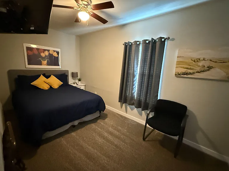 Furnished bedroom with a comfortable bed, nightstand, ceiling fan, and window with Blackout curtains for privacy.
