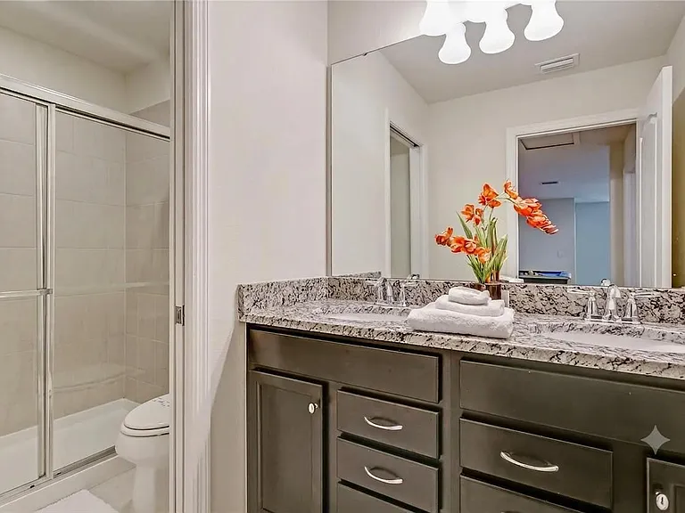 Bathroom with granite-top vanity, large mirror, and a glass-enclosed tub/shower combo for easy daily routines.