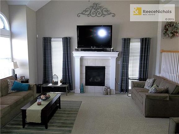 View of the large, vaulted Greatroom with a bank of windows on the left and windows on either side of the fireplace.