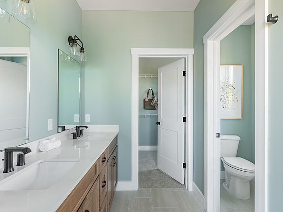 A clean, contemporary bathroom featuring double sinks, large mirrors, and soft green walls, with an