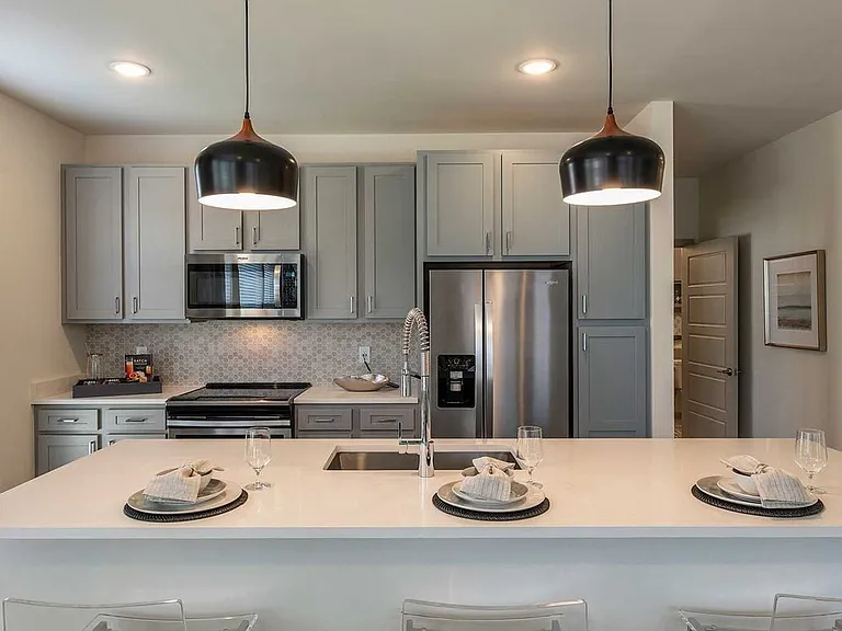 East Classic I kitchen with grey cabinetry, white granite countertops, stainless steel appliances, grey honeycomb tile backsplash, and hard surface plank flooring