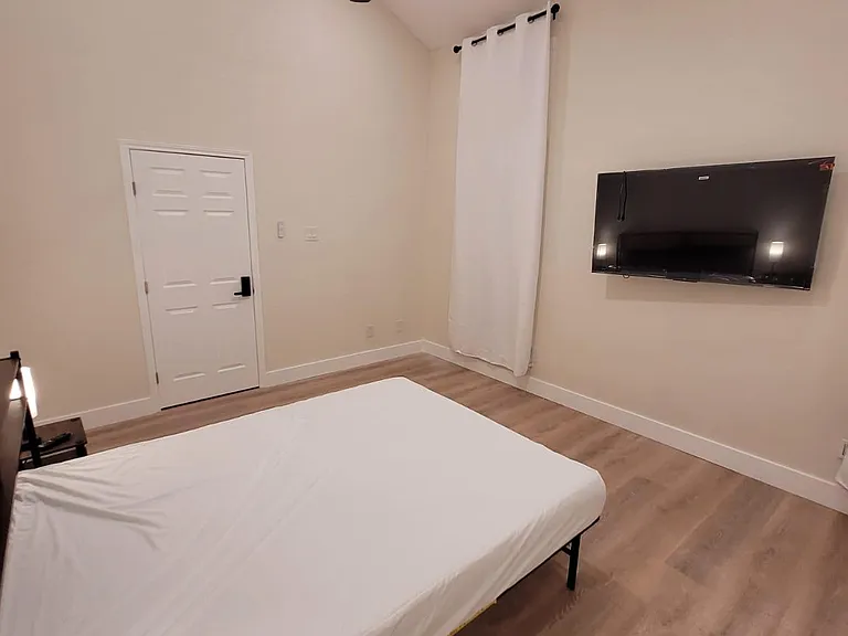 Bedroom features high ceilings, wood-look flooring, a ceiling fan, and a wall-mounted TV for easy lounging.
