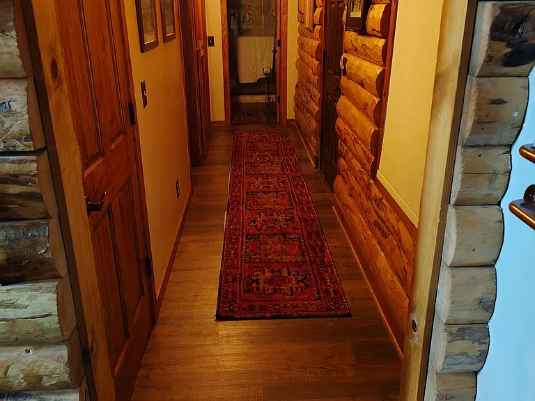 Warm wood hallway with plank flooring, sconce lighting, and rustic log accents connecting rooms and bath access.