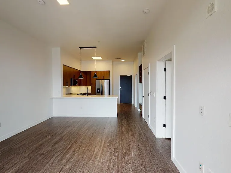 Apartment kitchen with stainless steel appliances, dining and living room with wood-style flooring.