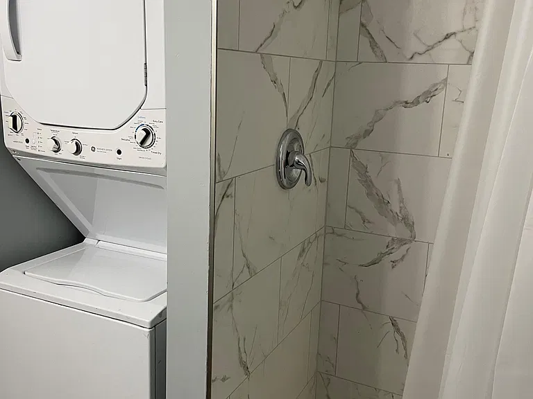 Tile shower stall with modern wall tile and hex floor, plus convenient in-home stacked washer and dryer nearby.
