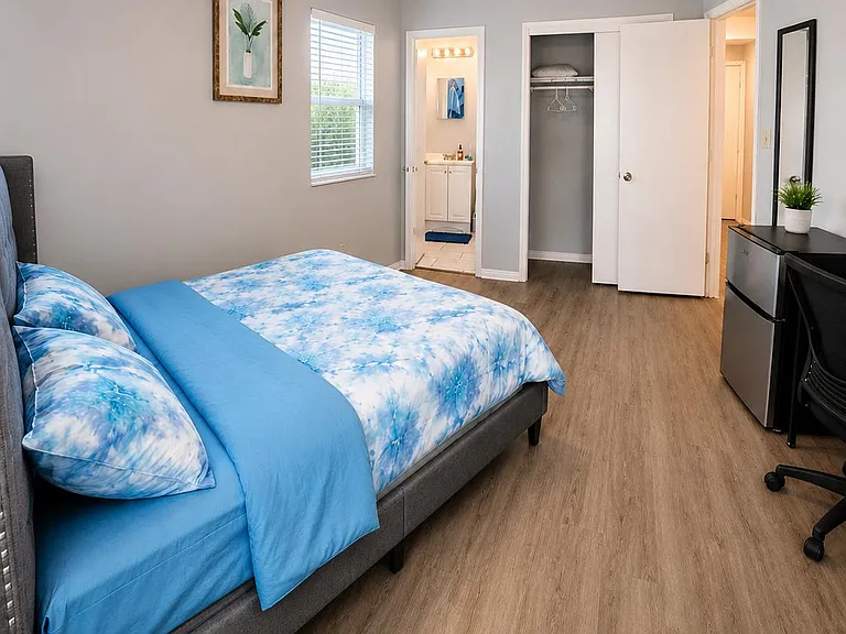Furnished bedroom with wood-look flooring, ceiling fan light, a dedicated desk area, closet storage, and nearby bath access.