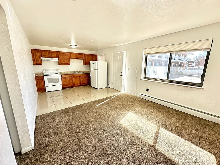 Bright and inviting open-concept living room with a modern kitchen featuring wooden cabinets and large window views.