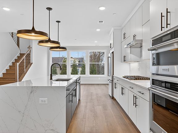 A modern, open-concept kitchen with white cabinets, stainless steel appliances, and pendant lighting