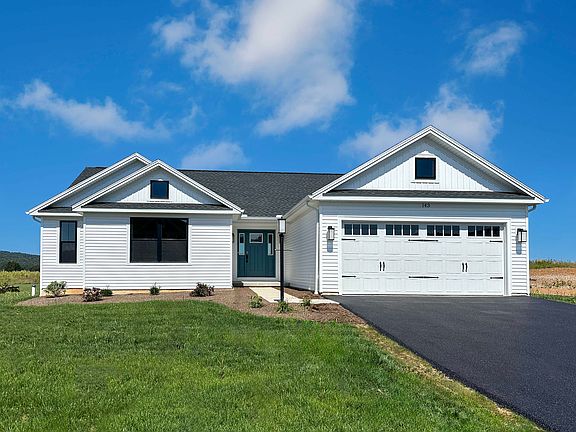 White ranch-style home with black roof, teal front door, two-car garage, and landscaped yard, set ag