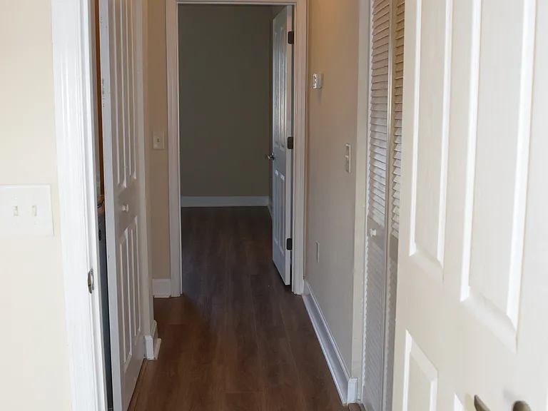 Hallway between primary and second bedrooms with laundry to the left and A/C utility room with storage to the right.
