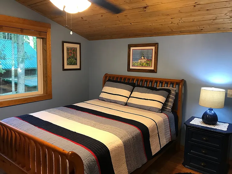 Bedroom with queen size bed, overhead ceiling fan/light and 3 drawer nightstand.