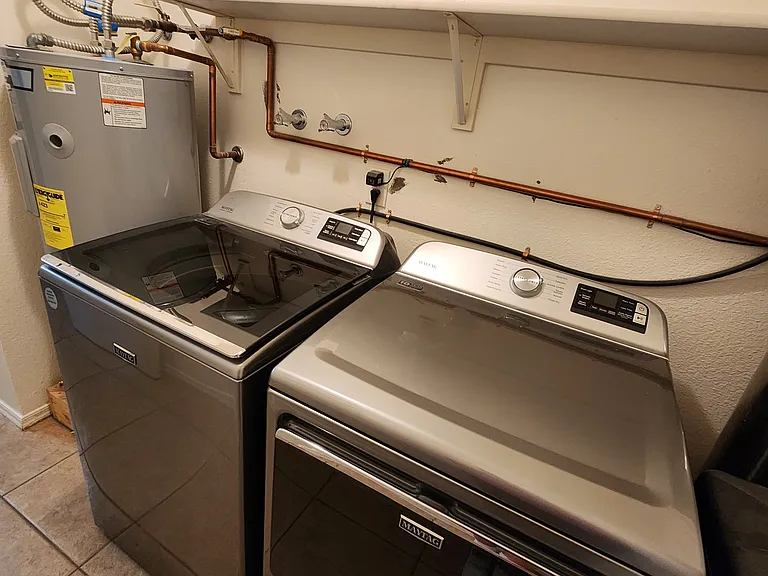 Modern inside laundry with large clothes washer dryer and whole home water softener softener.