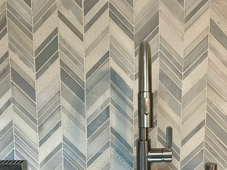 Nickel finish faucet with pull-down handle. Marble mosaic backsplash