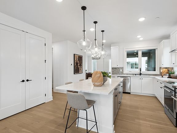 A modern, open-concept kitchen with white cabinets, a central island, and pendant lighting fixtures,
